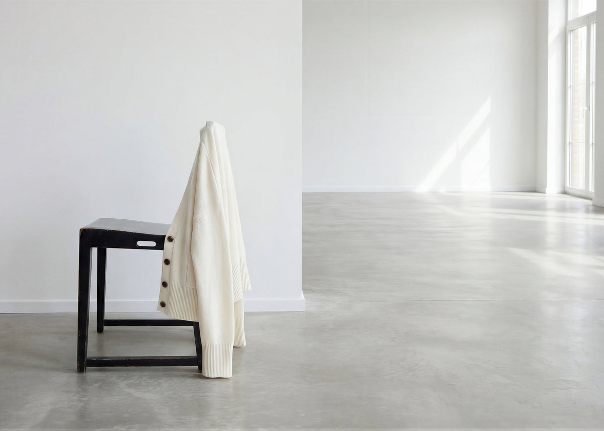 White coat draped over a black chair in a minimalistic room with concrete floor and large windows.