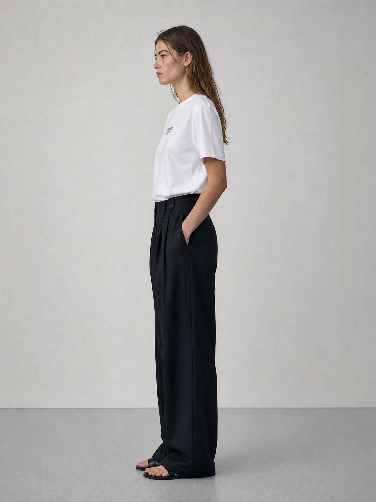 Woman wearing a white t-shirt and black pants against a plain background