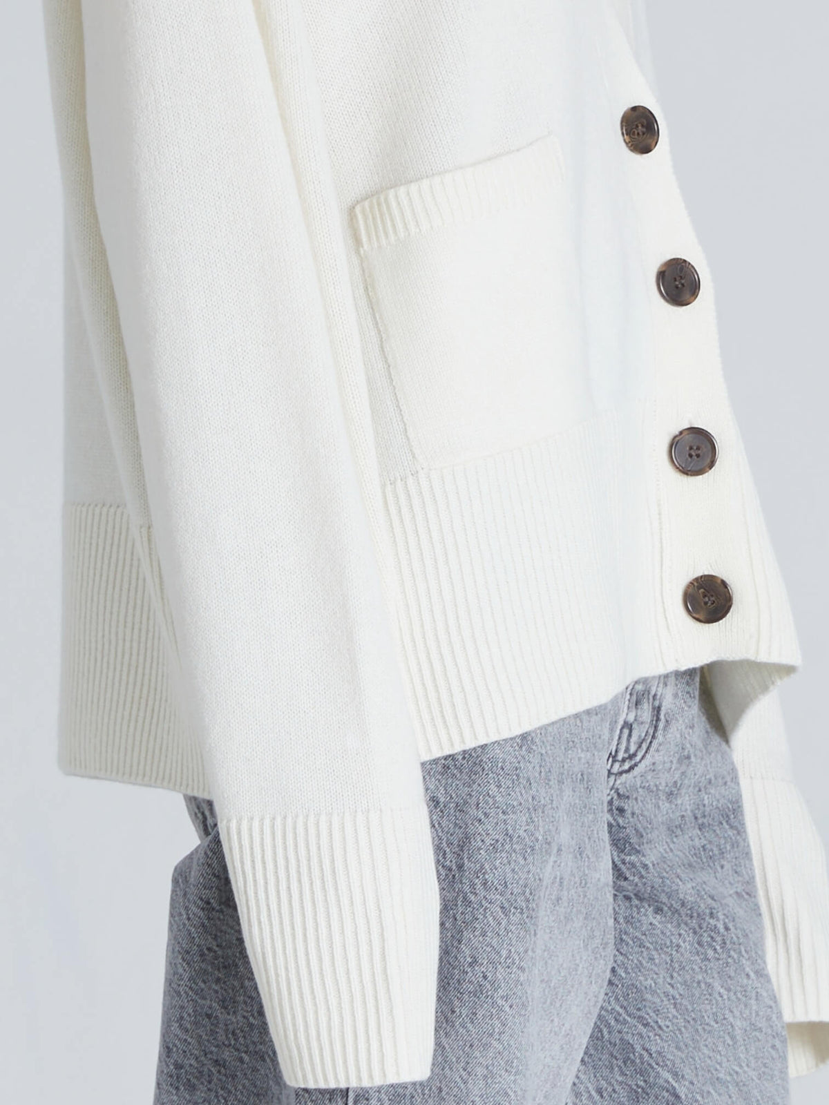 White cardigan with brown buttons over gray pants on a white background